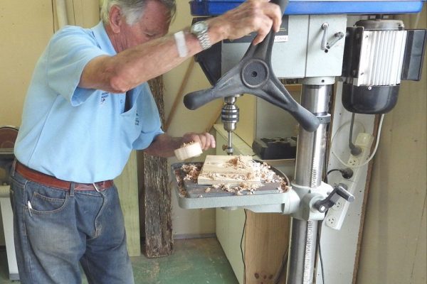 John inspects his work after drilling the circular window in the car body, using the drill press.